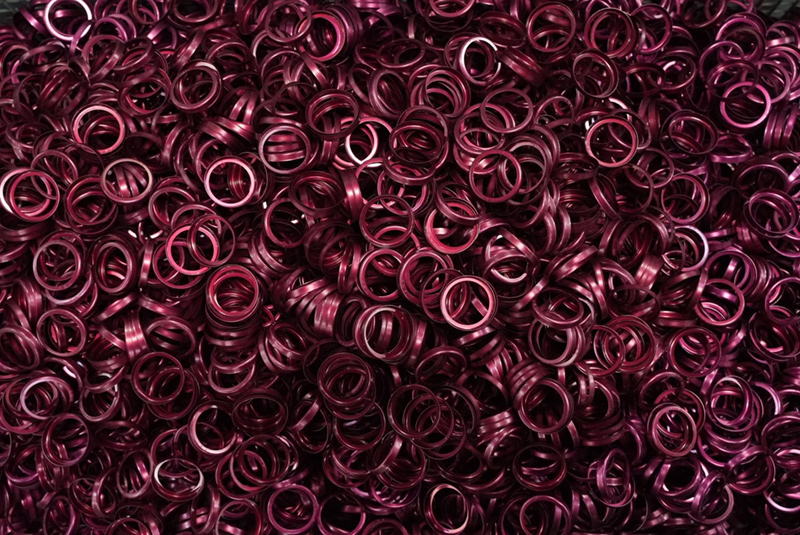 A large pile of anodized metallic, shiny, magenta-colored rings.