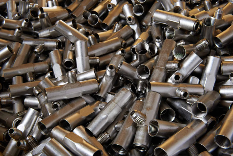 A large pile of shiny, electroless nickel cylindrical metal pipe fittings with threaded ends,