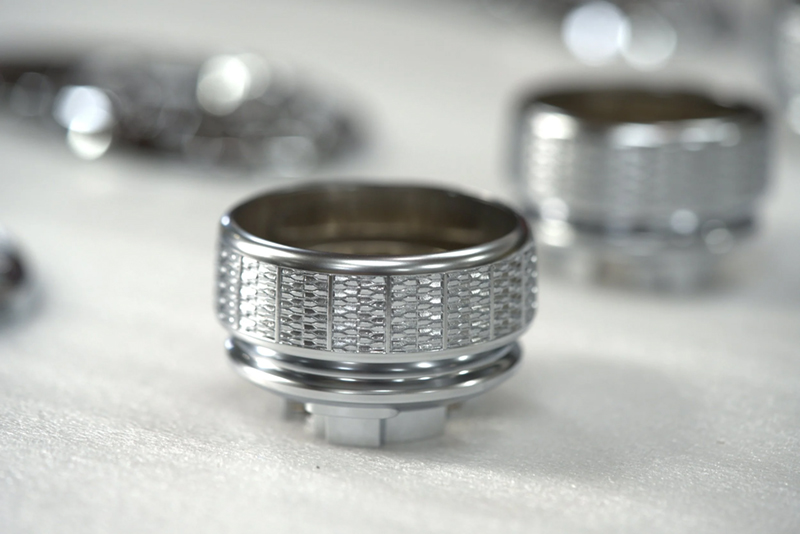 A close-up of a satin nickel, textured circular object with detailed ridges