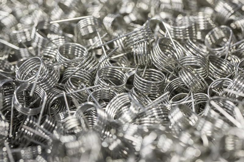 A close-up view of many shiny metallic springs piled together, creating a dense, tangled texture with reflective silver surfaces.